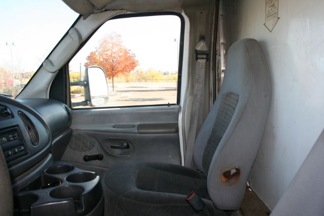 Ford E-350 cargo van interior cabin view with gray driver seat and empty cargo area side wall.