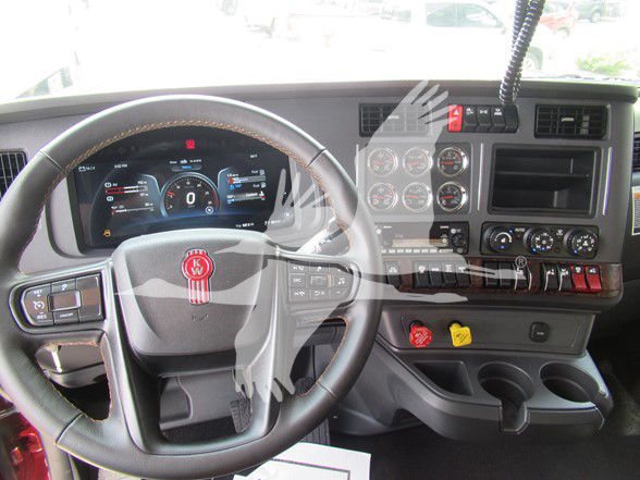 Conventional sleeper truck cockpit with steering wheel and dashboard controls visible; Kenworth emblem on steering wheel and instrument cluster in view.