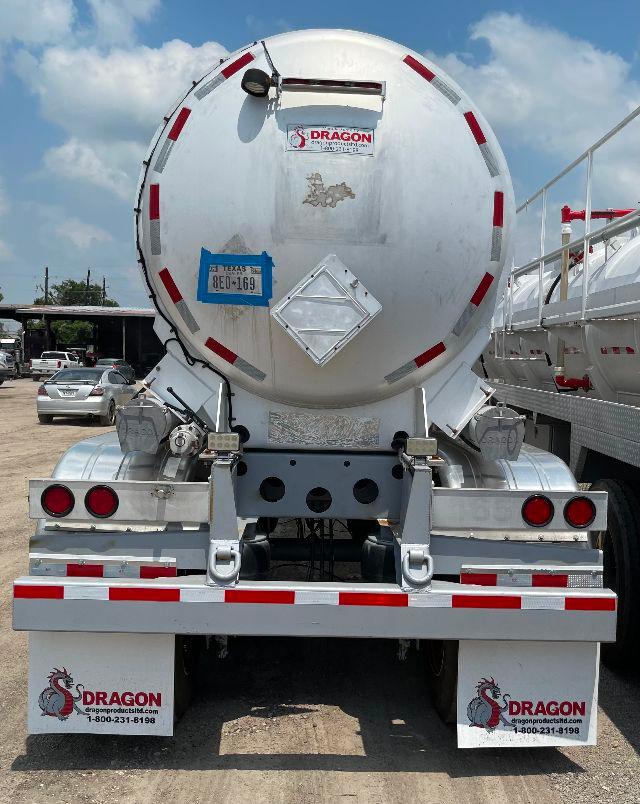 Rear view of a 2012 aluminum DOT-407 crude oil tanker trailer with Dragon branding, blue Texas license plate, decals, and brake lights.