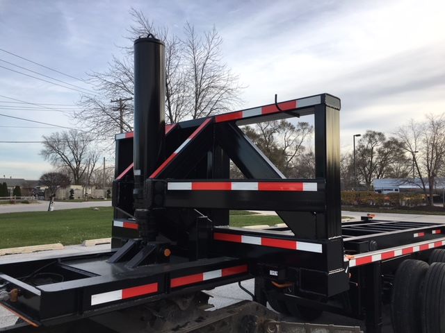 Black trailer chassis with a vertical support and hydraulic mechanism, red and white reflective stripes, and stacked framework, no visible text.