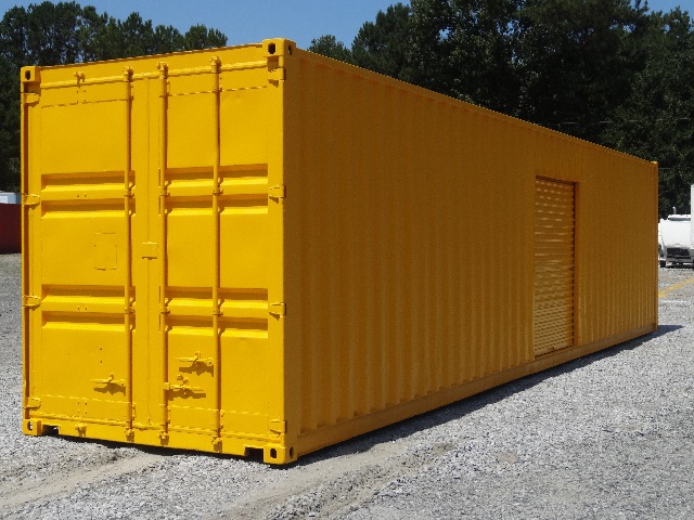 Yellow shipping container trailer with roll-up door on one side and double doors at the rear, set on gravel with trees in background.
