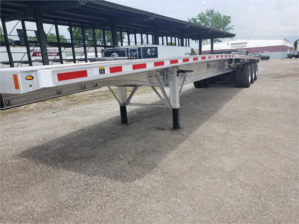Flatbed trailer showing all-aluminum Fontaine Revolution 52 with tri-axle configuration and reflective safety stripes.