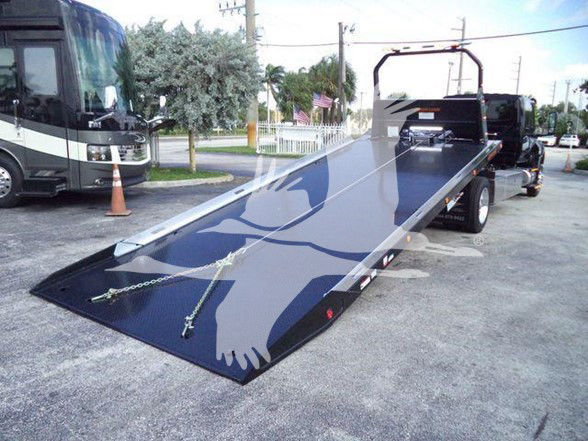Flatbed tow truck with long black steel ramp on a trailer, International MV stock image with watermarked silhouette.