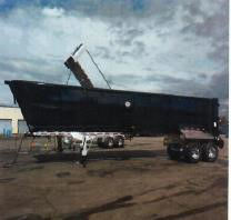 Trailer showing a 2023 40ft steel frameless half round dump on a dual-axle trailer with the dump bed raised, parked on a lot.