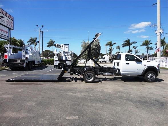 2024 Ram 5500 HD hooklift truck with a long tilt bed and hydraulic lifting arm.