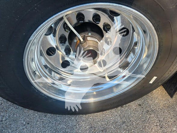 Wheel and tire assembly on a flatbed trailer showing polished steel rims with multiple circular holes and lug nuts.
