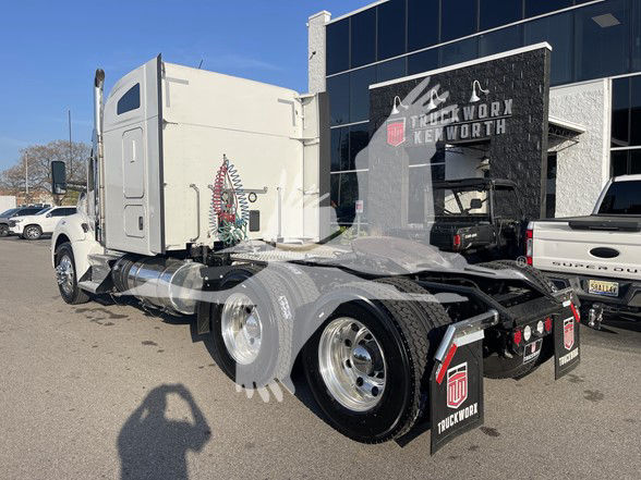 Kenworth T880 truck chassis rear view showing cab with sleeper, white color, chrome wheels, dual rear axles, mud flaps with TruckWorld logo, dealership building in background.
