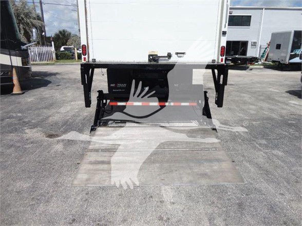 Truck rear with ramp/loading platform and hydraulic lift system visible under a white box body; tailgate open in loading position.