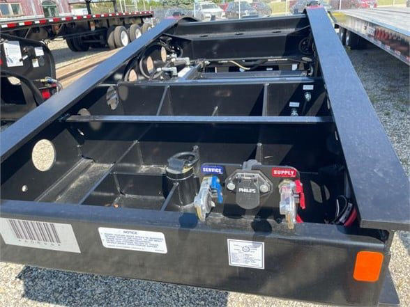 Lowboy trailer frame with visible valves labeled SERVICE and SUPPLY, hoses, and wiring; steel construction; front deck area with access compartments.
