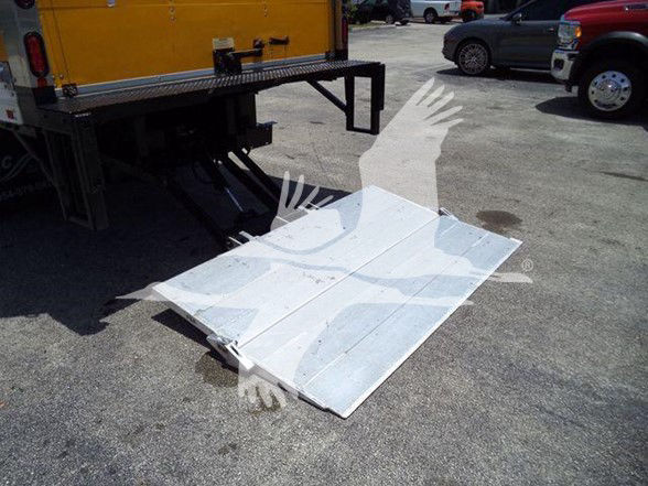 Platform drop-down ramp or liftgate sheet metal on the ground with a yellow truck in background.