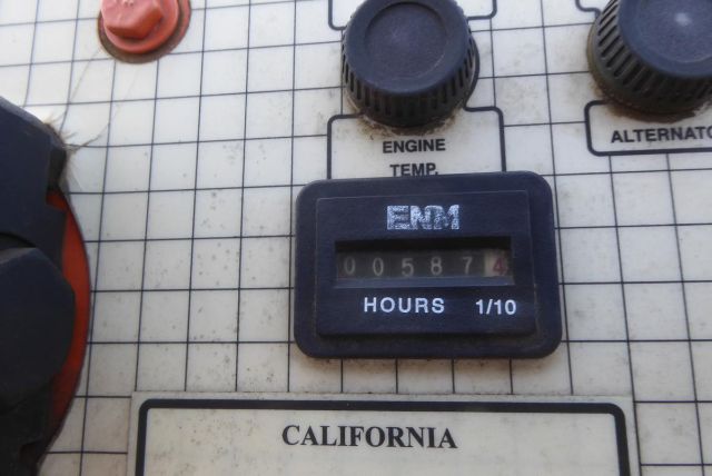 Trucking equipment control panel showing an HOURS 1/10 odometer labeled EM, with engine temperature labels and a California placard.