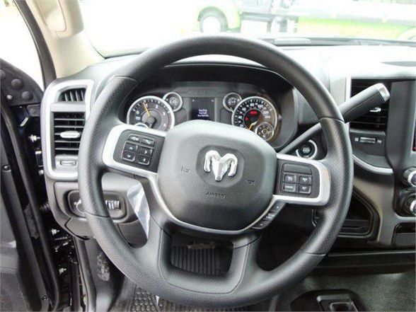 Ram steering wheel with RAM logo center; dashboard gauges visible behind; left and right stalks; steering wheel buttons; interior of a Ram truck.
