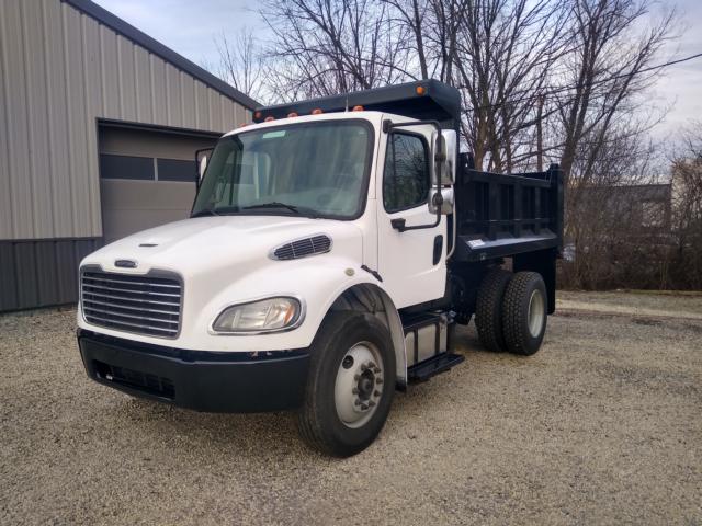 White Freightliner M2 dump truck with black dump bed, front grille, and dual rear tires in a gravel lot.