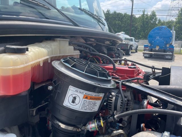 Freightliner M2 engine bay showing air inlet manifold heater and coolant reservoir with hoses and wiring.
