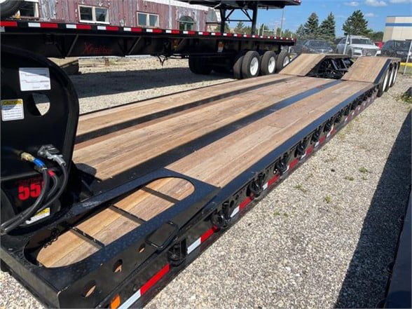 Lowboy trailer with long wooden deck and multiple axles, 55-ton Fontaine steel roller paver trailer, black painted steel frame, side ramps and tie-downs visible.