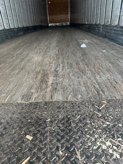 Interior of a trailer showing wood floor and diamond plate threshold; empty cargo area with metal walls.