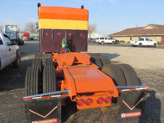 Kenworth truck tractor rear view showing orange chassis and dual rear axles, mud flaps with Kenworth logos.