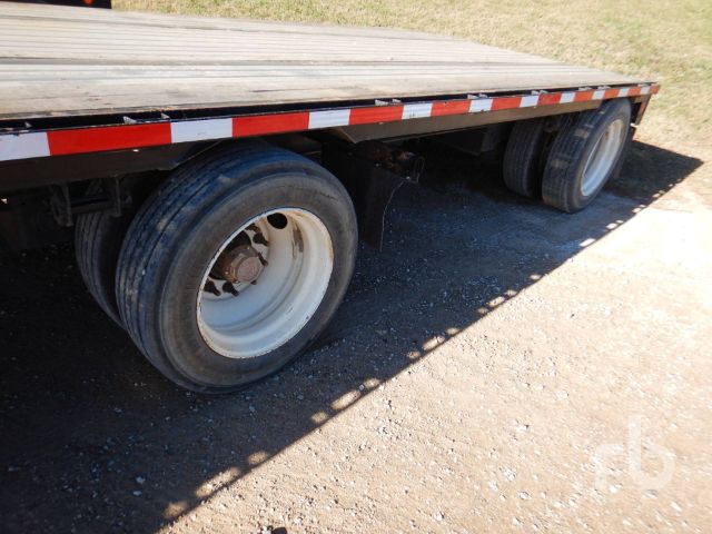 Trailer wheel area showing two axles with dual tires and white steel rims. Side railing with red and white reflective tape.