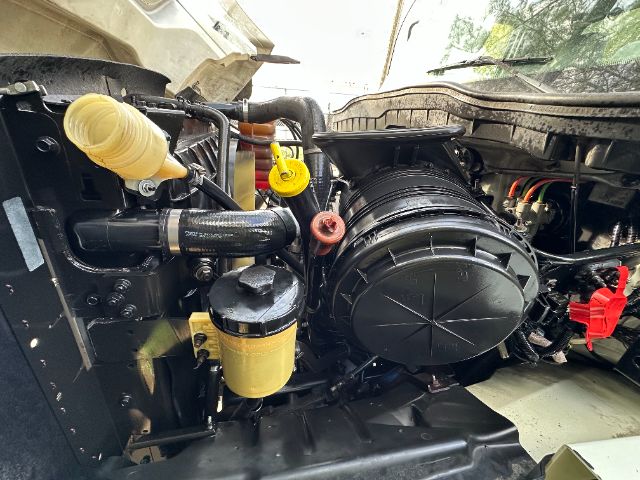 Interior of engine bay on a 2014 International 7500 vacuum truck showing black circular air intake housing, yellow coolant reservoir cap, yellow dipstick/handle, red cap, and various hoses.