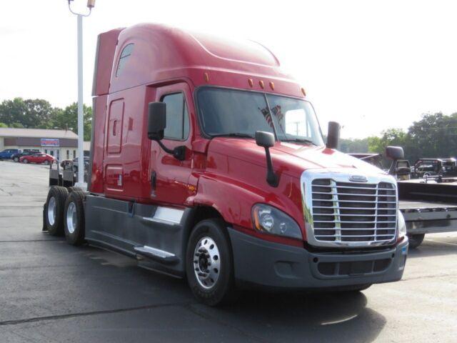 Truck cab showing a red Freightliner Cascadia Evolution with chrome grille, sleeping berth, and dual rear axles.