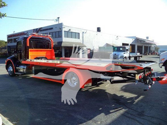 Kenworth T280 flatbed tow truck in a dealership lot; side view with orange and black color scheme, wheel rims, and dealership building in background.