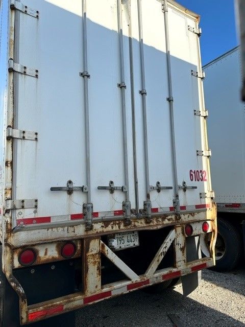 Rear view of a white Wabash Duraplate trailer with doors closed, rusted bumper, red and white reflective tape, and trailer number 61032.