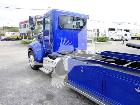 Blue 2022 Peterbilt 337 tow truck cab and chassis with extended blue wheel well, visible rear storage compartments, and black tonneau area.