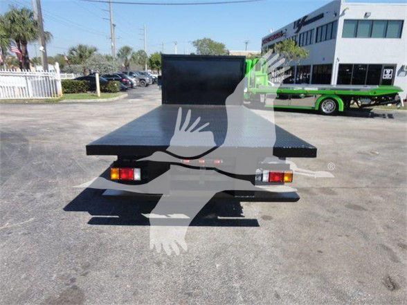 Truck flatbed with green tow truck in background; rear view showing flatbed platform and taillights.