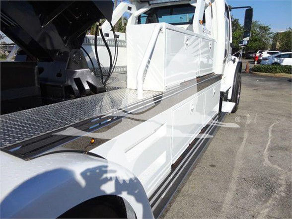 Tow truck side view showing white Freightliner BUSINESS CLASS M2 106 with open service body and diamond plate steps.