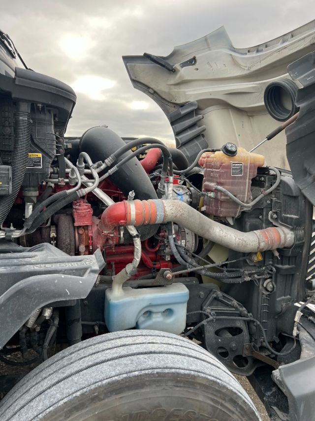 Engine bay of a 2019 International LT625 truck showing red engine block, large orange radiator hoses, coolant reservoir, and blue windshield washer reservoir.