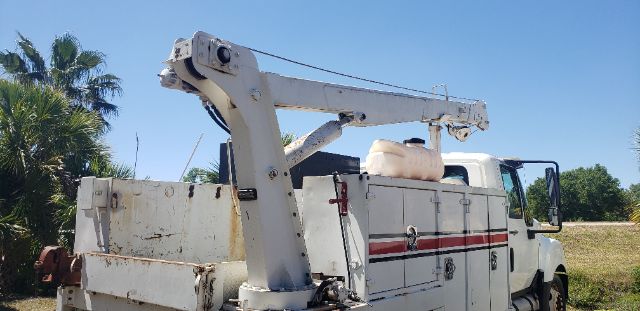 Ford F-550 utility truck with hydraulic lift/boom in bed and white paint with red stripe. Side cabinets and equipment mounted in bed.