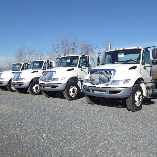 Fleet of white International 7400 SBA trucks parked on gravel lot with blue sky.