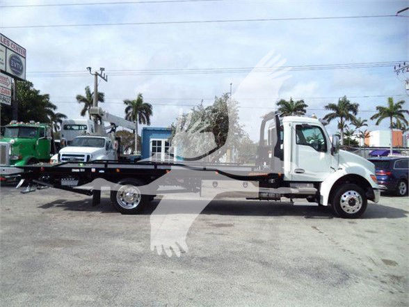 Kenworth T280 tow truck flatbed in a dealership lot, white cab and black flatbed, palm trees in background.