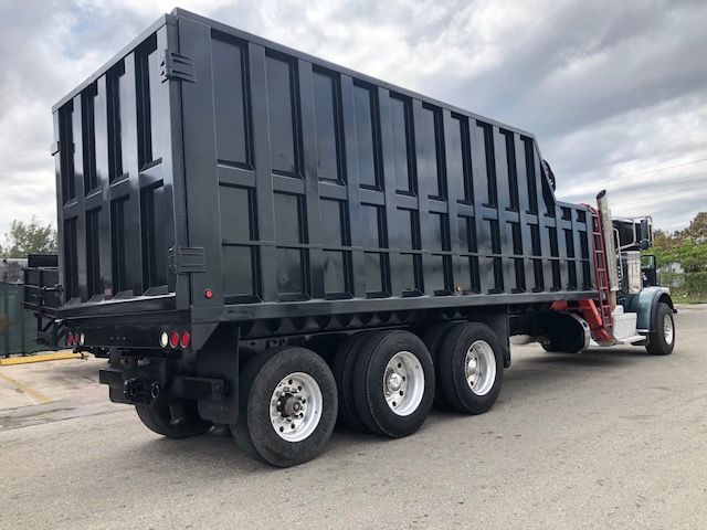 Peterbilt 388 dump truck with a large black dump body, triple rear axles, and a light blue cab.