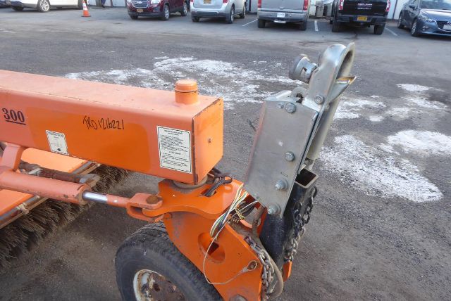 Orange Laymor SM300 truck implement with hydraulic component and steel mounting bracket, visible VIN plate area, and warning label on orange housing.
