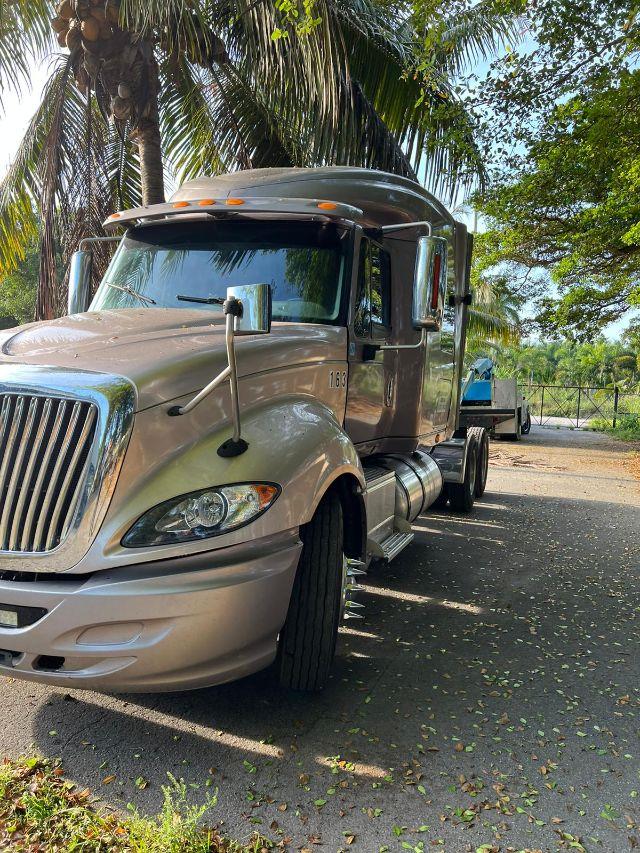 International Prostar truck front-left angle showing cab and sleeper, beige color, chrome grille, large mirrors, and sun visor.