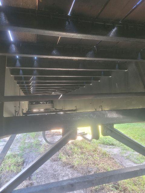 Trailer underside showing frame rails and support beams with a view through to the ground and grass; no readable labels or stickers.