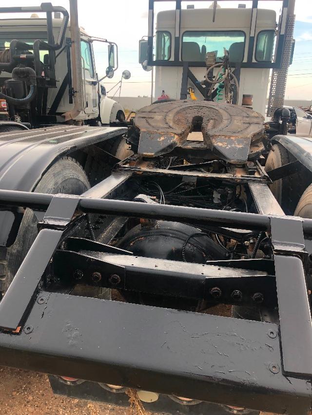 Kenworth truck chassis with exposed drivetrain and fifth-wheel coupling showing various hoses and metal framing.