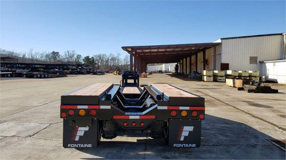 Fontaine lowboy trailer rear view showing flatbed with black frame, red and amber taillights, Fontaine logos on mudflaps.