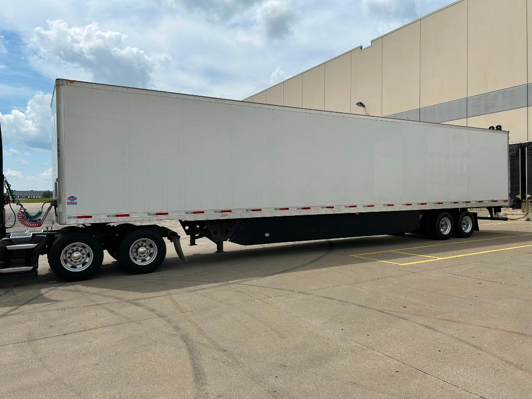 Side view of a white semi-trailer attached to a tractor, parked in a lot.