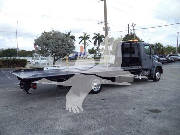 Tow truck with a flatbed trailer attached, cab is dark gray, parked in lot.
