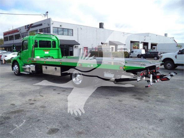 Green Peterbilt tow truck with flatbed side view showing equipment and truck bed