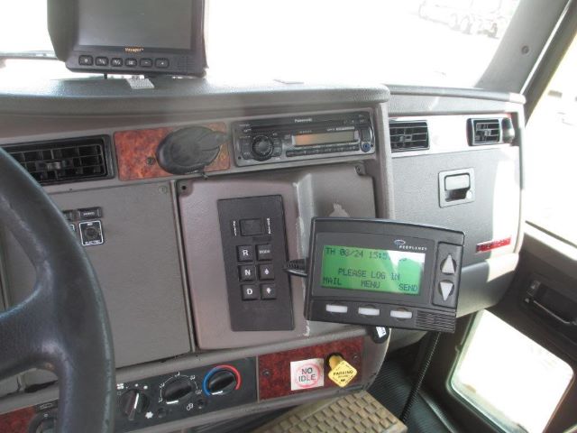 Kenworth T300 truck interior showing dashboard with gear selector, monitor, and a green LCD message device attached to the dash.