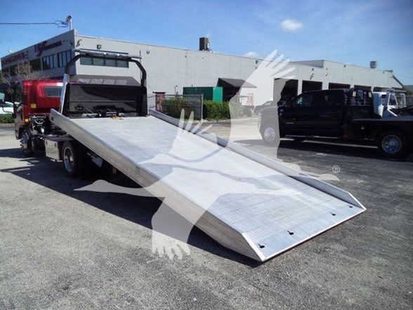 Isuzu NPR XD tow truck bed with lowered ramp in foreground and other vehicles in background.