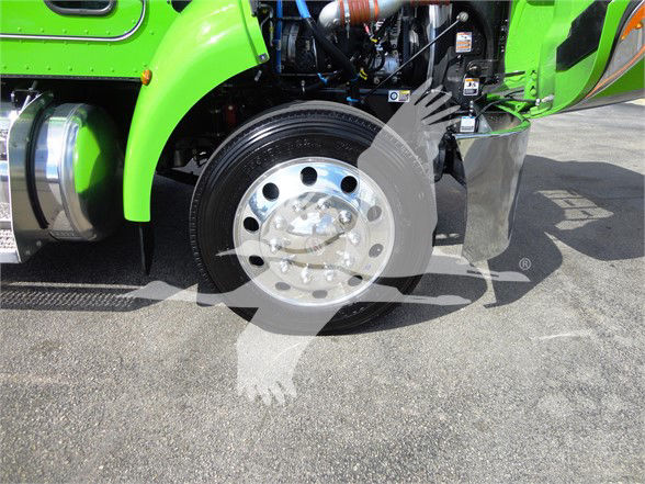 Front wheel well of a lime green Peterbilt 337 truck showing polished aluminum wheel with multiple circular lug holes and surrounding engine components.