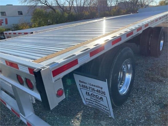 Flatbed trailer with aluminum deck and dual rear axles; new Fontaine Revolution 52-53ft flatbed trailer with reflective tape and rear lights visible.