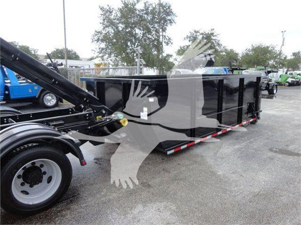 Truck trailer bed with black side walls and rear reflective tape, attached to a blue-framed hitch on a gravel lot.