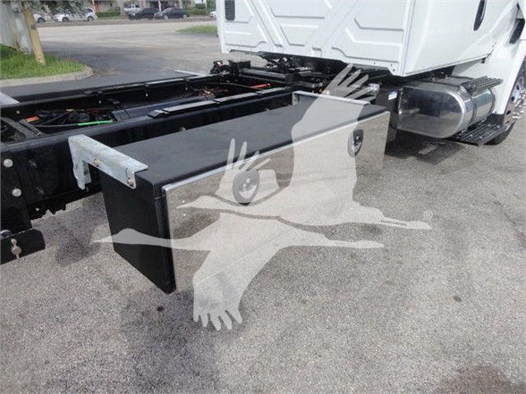 Truck chassis with a black rectangular toolbox mounted over the frame near the cab; white truck cab in background.