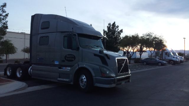 Volvo 780 conventional sleeper truck parked in a lot with front grille, cab high roof, and multiple trailers in background.