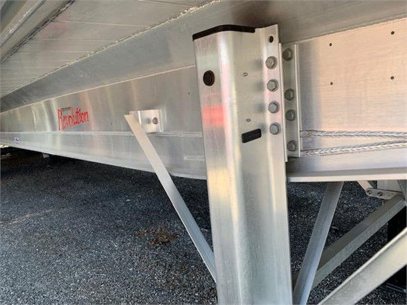 Trailer undercarriage showing aluminum frame and support leg with bolt holes and safety chains.